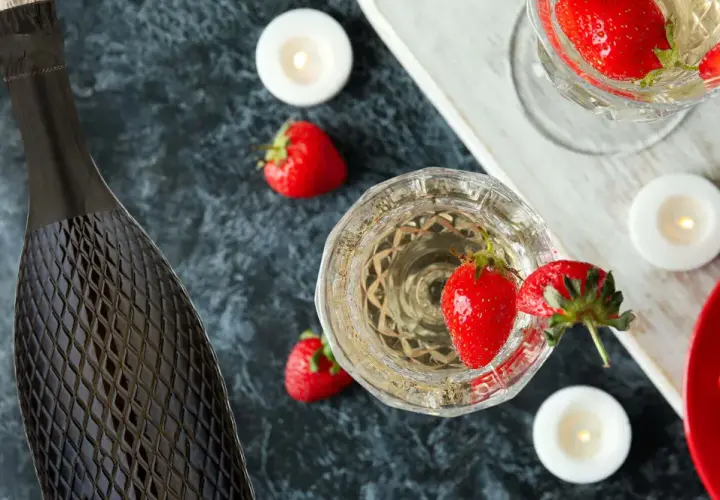 Butelka i kieliszki pełne musującego prosecco, ozdobione truskawkami i świecami. Idealne na romantyczny wieczór.