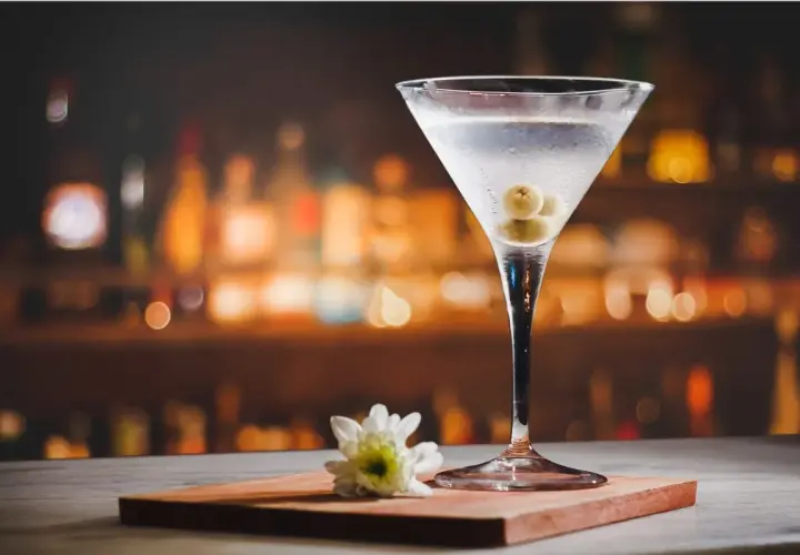 Kieliszek martini z oliwkami i kwiatkiem na tle rozmytego baru. Idealny dodatek do wieczoru, z czym pić martini?