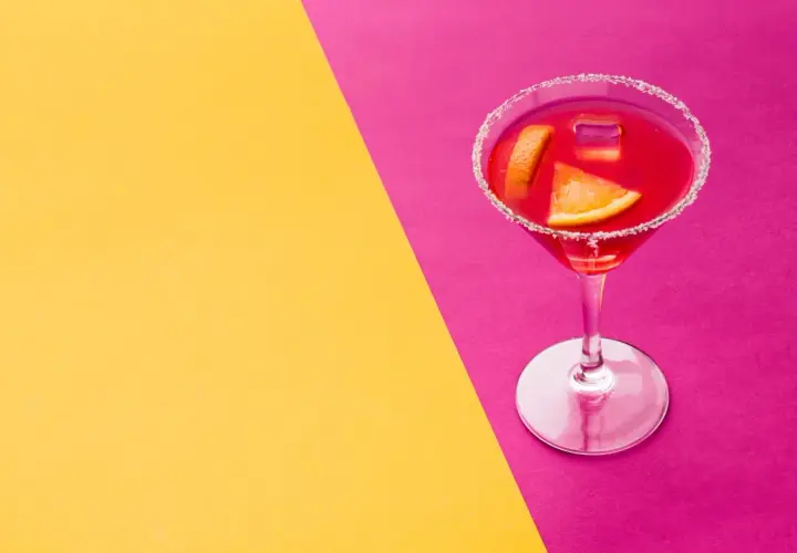 Elegancki kieliszek z czerwonym drinkiem, ozdobiony plasterkami pomarańczy i cukrowym rantem, idealny na wieczór w stylu cosmopolitan.