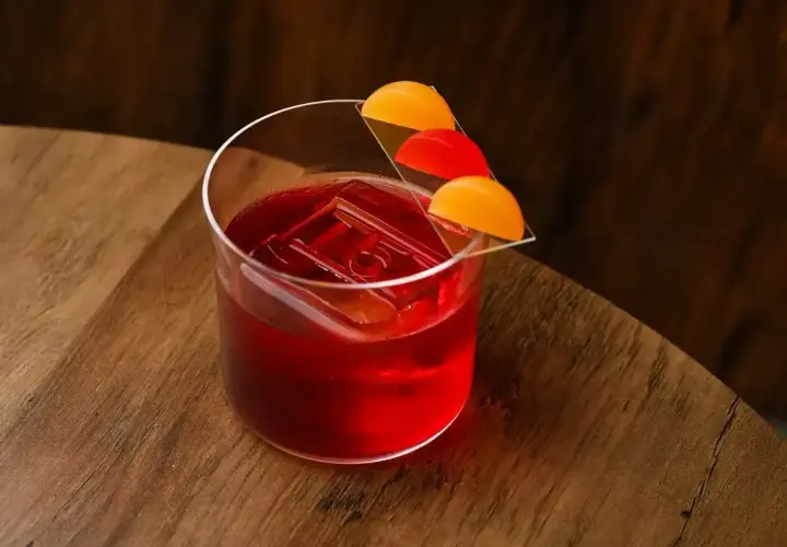 Czerwony koktajl Negroni z lodem i plasterkami pomarańczy na szkle.