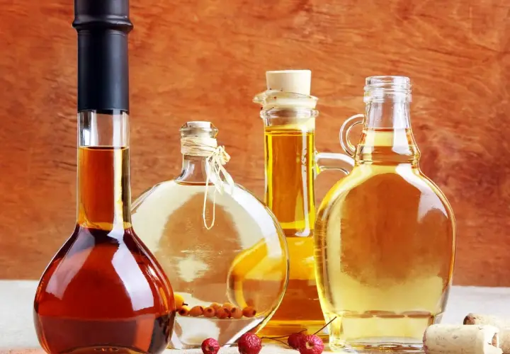 Cztery butelki z płynami: ciemny alkohol, jasny płyn z owocami, złoty olej i miodówka.