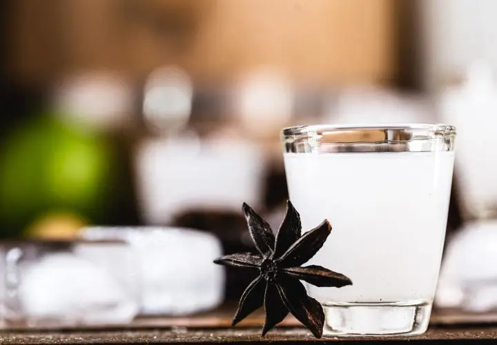 Mętny arak w szklance, obok gwiazdka anyżu i kostki lodu.