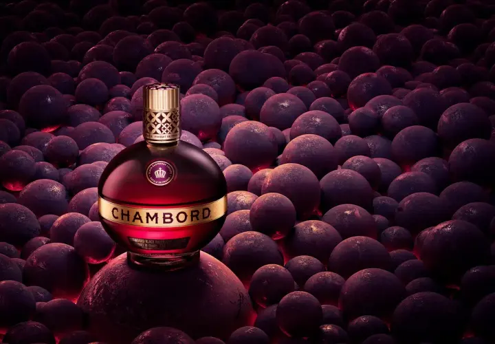 Elegancka butelka likieru Chambord wśród ciemnych, okrągłych owoców, emanująca luksusem i bogactwem smaku.