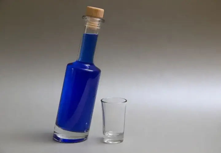 Niebieski likier w butelce z korkiem i pusty kieliszek.