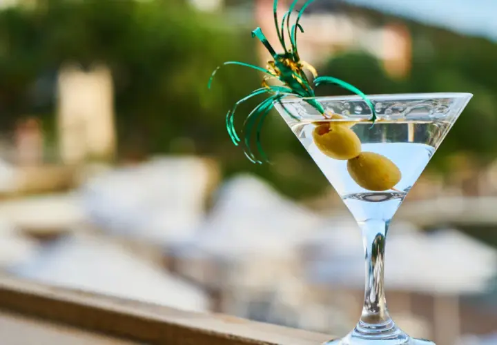 Orzeźwiający martini fiero z oliwkami, ozdobiony zieloną wstążką, na tle rozmytego, letniego krajobrazu.