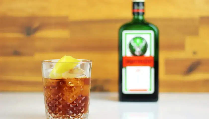 Szklanka z drinkiem i cytryną obok butelki Jägermeister. Ten jager alkohol to idealny dodatek do wieczoru.