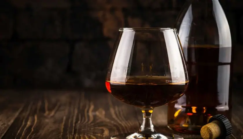 Kieliszek brandy i butelka na drewnianym stole. Idealny moment, by zastanowić się, z czym pić brandy.