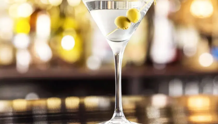 Kieliszek martini z dwiema oliwkami na wykałaczce na tle rozmytego baru.
