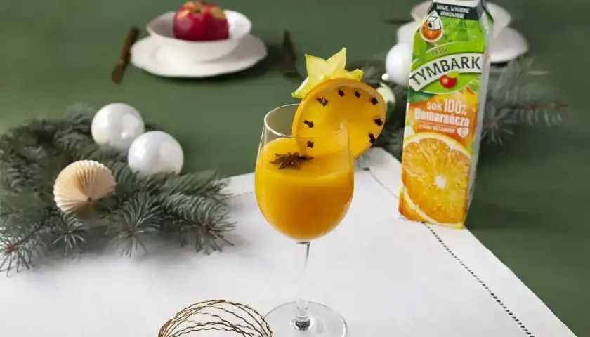 Pomarańczowy koktajl w kieliszku, ozdobiony plasterkiem pomarańczy z goździkami i gwiazdką anyżu.