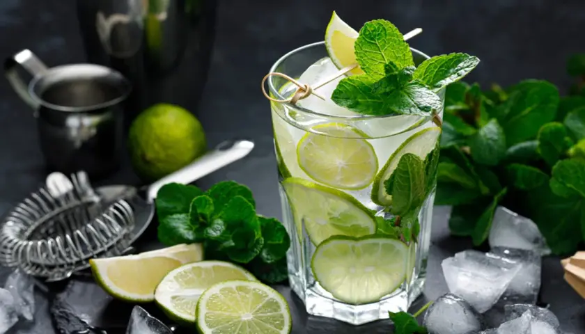Szklanka orzeźwiającego mojito z limonką i miętą, otoczona lodem i składnikami.