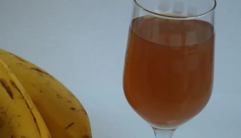 Dwa banany obok kieliszka z bursztynowym płynem.