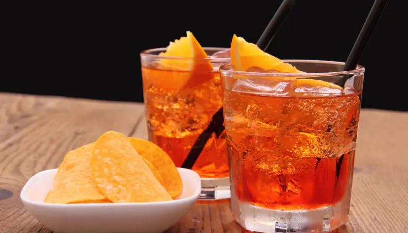 Dwa orzeźwiające drinki z pomarańczą i słomkami, obok miseczka chipsów. Idealny aperitif na letnie popołudnie.