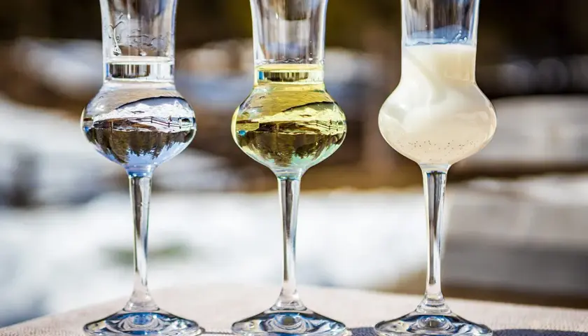 Trzy kieliszki z różnymi alkoholami, w tym jeden z mlecznym likierem.