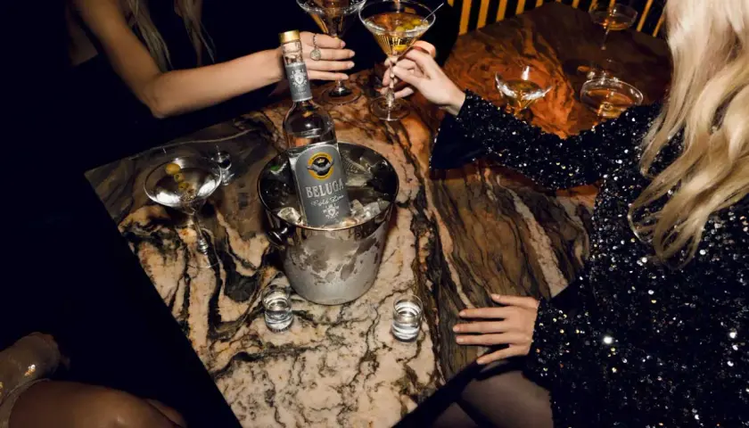 Butelka wódki Beluga w wiaderku z lodem, kieliszki z martini i shoty na marmurowym stole.