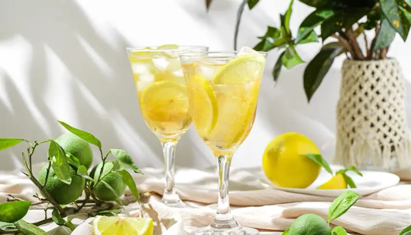 Orzeźwiający drink z limoncello, lodem i plasterkami cytryny, otoczony świeżymi owocami i zielonymi liśćmi.