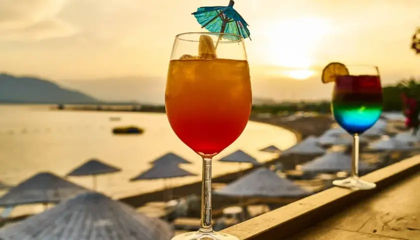Dwa kolorowe drinki na tle plaży i zachodzącego słońca.