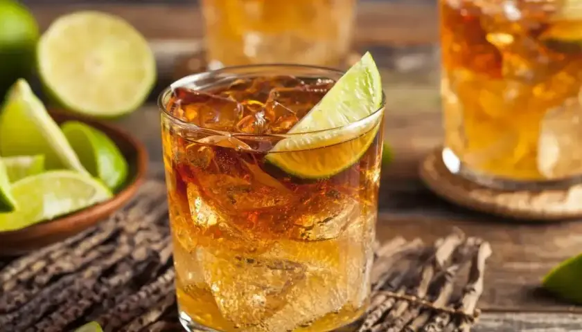 Szklanki z drinkami rumowymi z lodem i limonką, obok miseczka z ćwiartkami limonki.