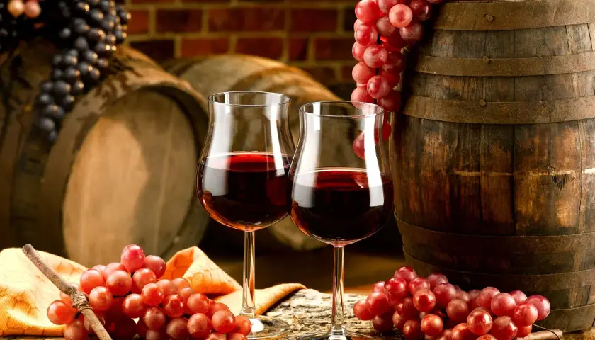 Dwa kieliszki czerwonego wina, winogrona i beczka. Czy wino może się zepsuć? Odpowiedź tkwi w jego przechowywaniu.