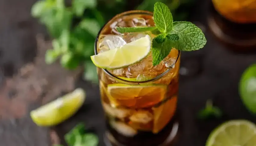 Szklanka z drinkiem z rumu Bacardi, lodem, plasterkami limonki i listkami mięty.