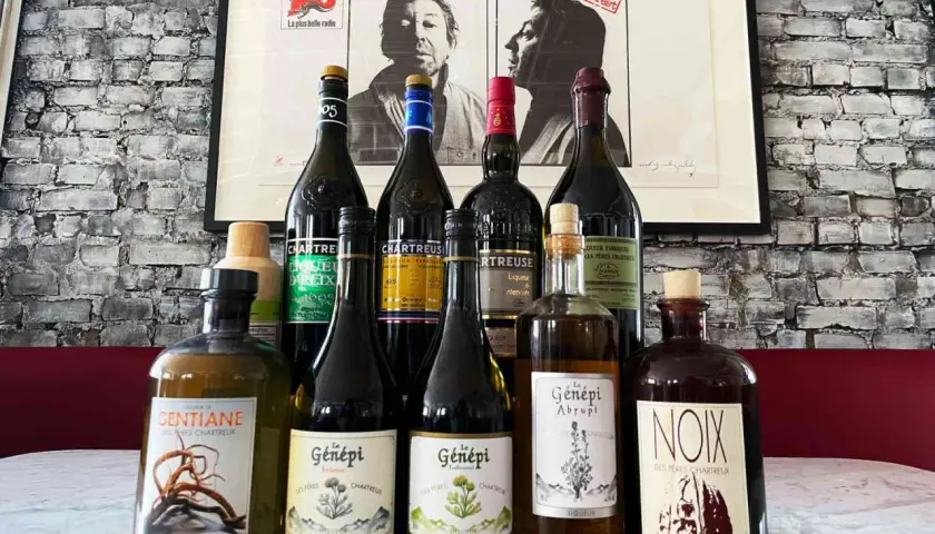 Butelki z zielonymi likierami Chartreuse i innymi francuskimi alkoholami na tle plakatu.