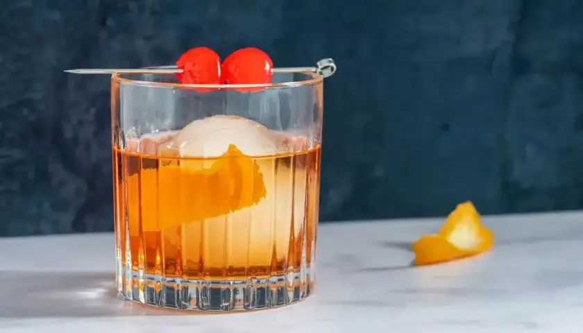 Klasyczny koktajl Old Fashioned z pomarańczą i wisienkami na patyczku.