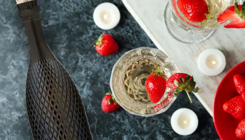 Butelka i kieliszki pełne musującego prosecco, ozdobione truskawkami i świecami. Idealne na romantyczny wieczór.