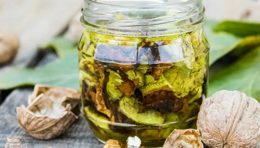 Nalewka z orzecha włoskiego na żylaki w słoiku, otoczona łupinami i orzechami. Naturalny sposób na wsparcie zdrowia.