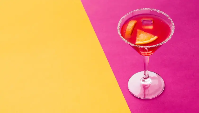 Elegancki kieliszek z czerwonym drinkiem, ozdobiony plasterkami pomarańczy i cukrowym rantem, idealny na wieczór w stylu cosmopolitan.