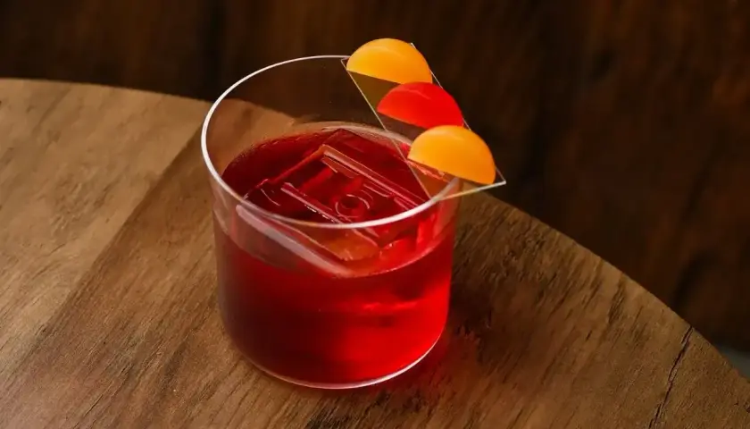 Czerwony koktajl Negroni z lodem i plasterkami pomarańczy na szkle.