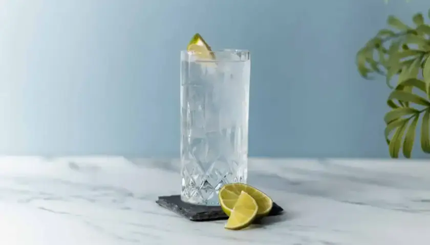 Szklanka z lodem i plasterkami limonki, ozdobiona limonką na brzegu.