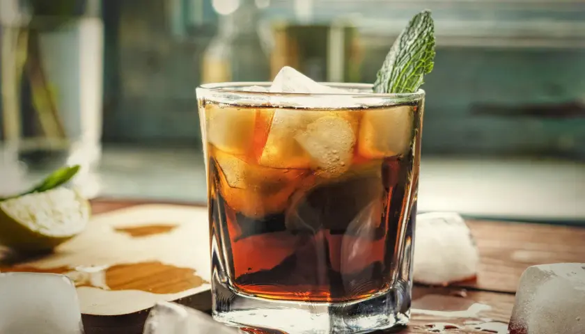 Orzeźwiający gin z colą, z kostkami lodu i listkiem mięty, na drewnianym blacie.