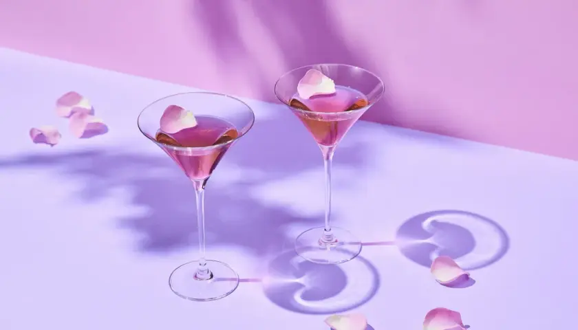 Dwa kieliszki z różowym Martini Rosso, ozdobione płatkami róż. Idealne na romantyczny wieczór. Z czym pić? Z dobrym towarzystwem!