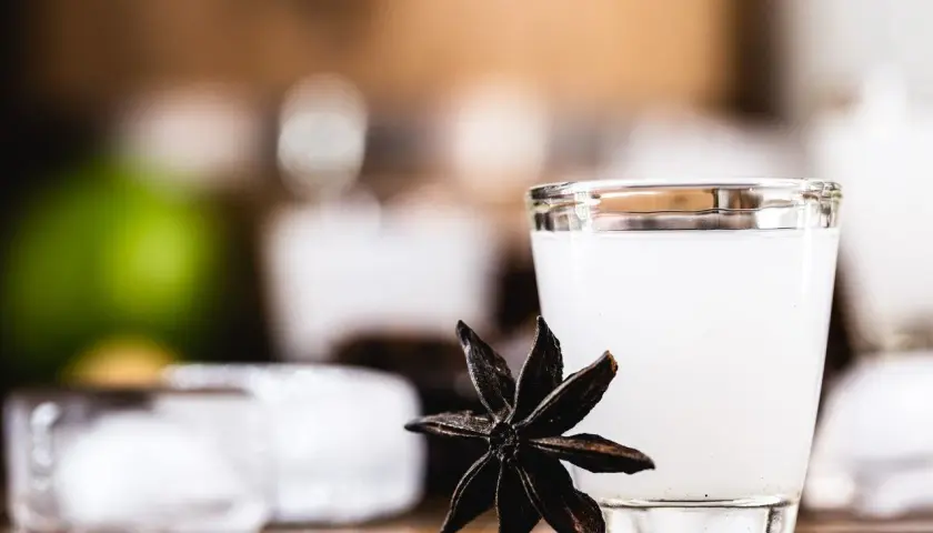 Mętny arak w szklance, obok gwiazdka anyżu i kostki lodu.