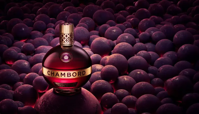Elegancka butelka likieru Chambord wśród ciemnych, okrągłych owoców, emanująca luksusem i bogactwem smaku.