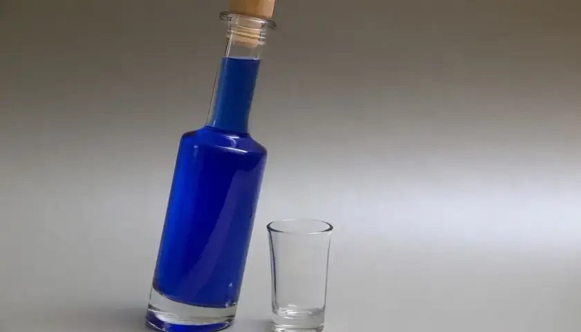 Niebieski likier w butelce z korkiem i pusty kieliszek.