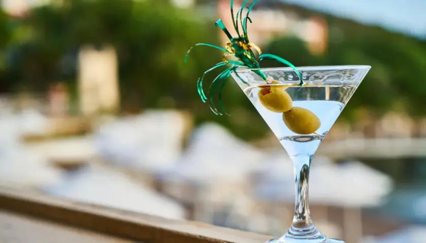 Orzeźwiający martini fiero z oliwkami, ozdobiony zieloną wstążką, na tle rozmytego, letniego krajobrazu.
