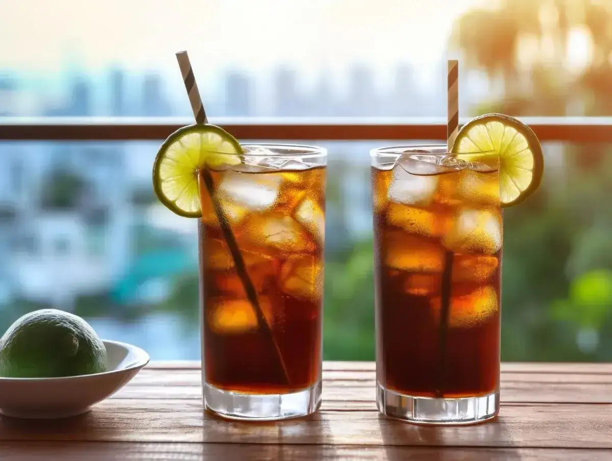 Dwa drinki Long Island Iced Tea z lodem, limonką i słomkami na drewnianym stole, z rozmytym tłem miasta.