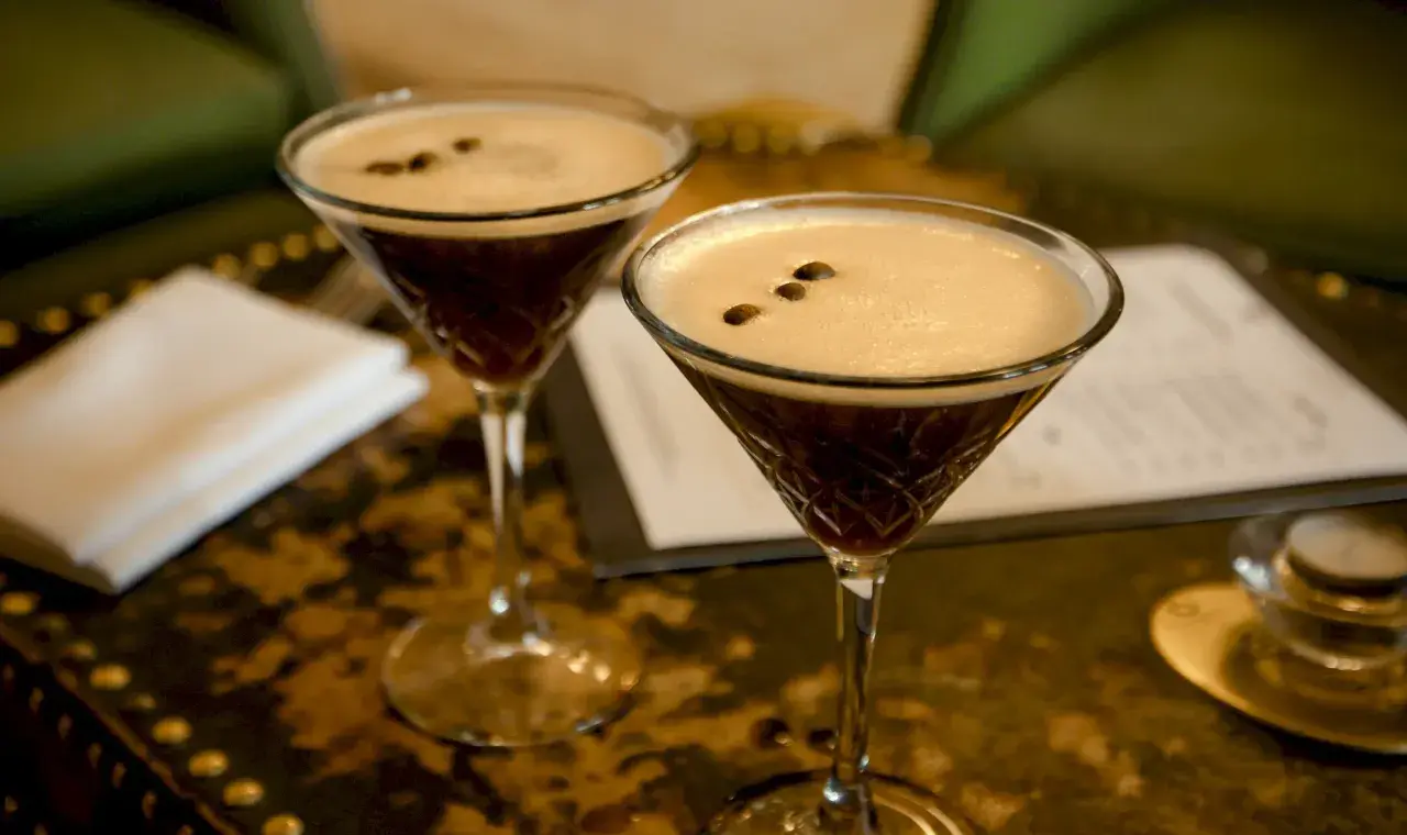 Dwa kieliszki Espresso Martini z gęstą pianką i ziarnami kawy na wierzchu.