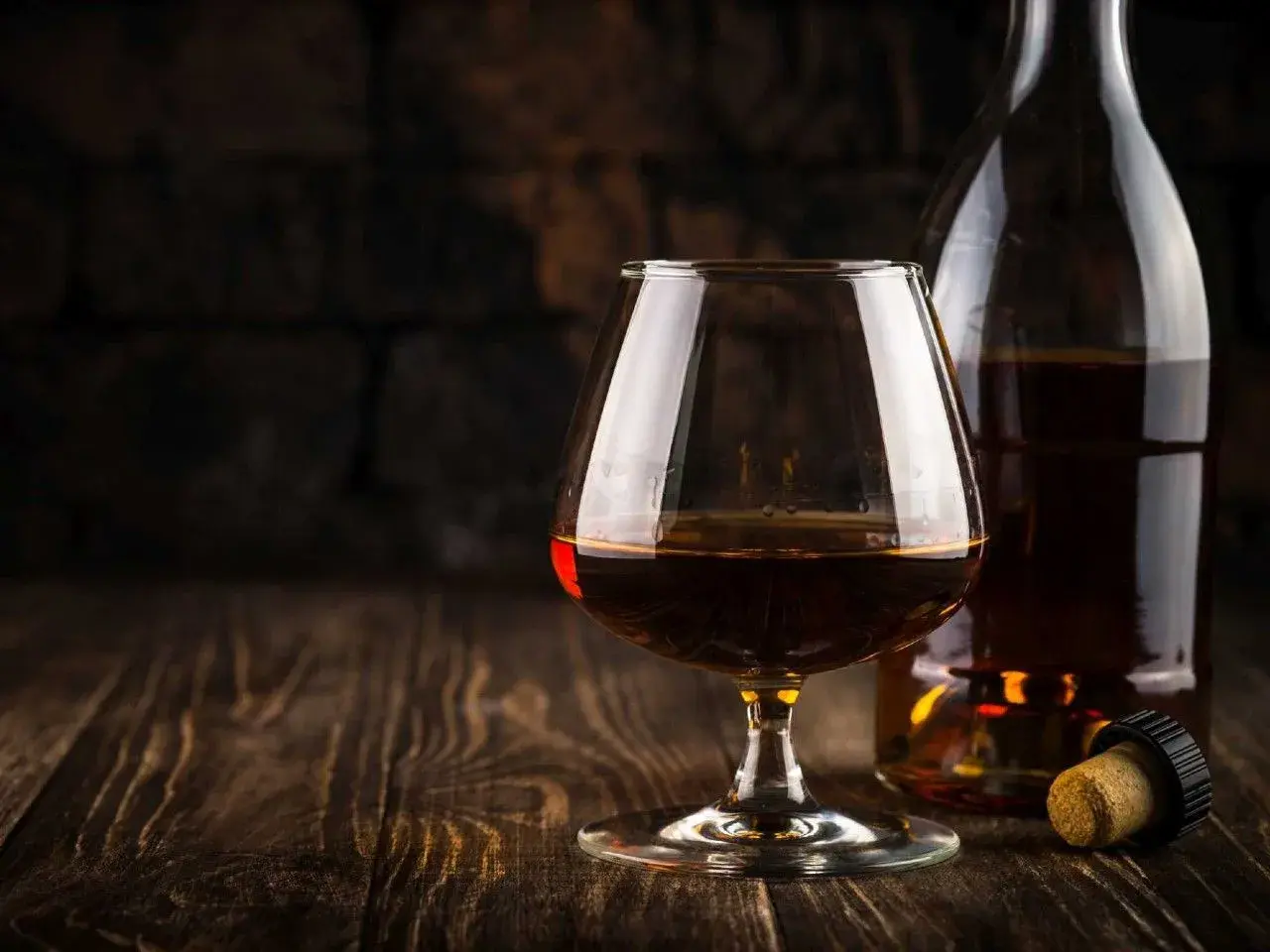 Kieliszek brandy i butelka na drewnianym stole. Idealny moment, by zastanowić się, z czym pić brandy.