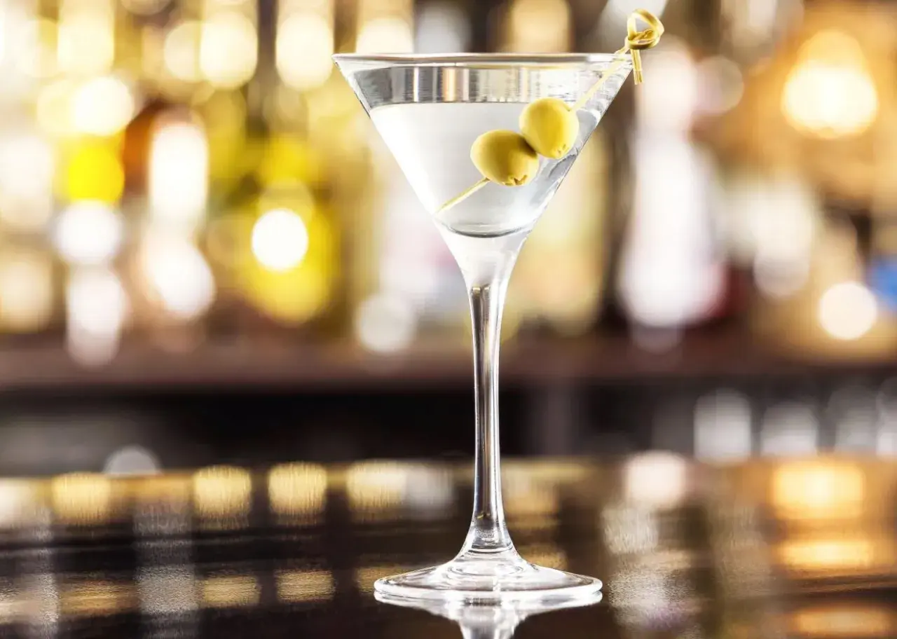 Kieliszek martini z dwiema oliwkami na wykałaczce na tle rozmytego baru.