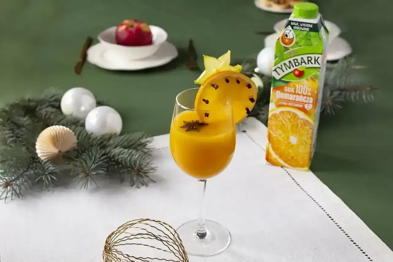 Pomarańczowy koktajl w kieliszku, ozdobiony plasterkiem pomarańczy z goździkami i gwiazdką anyżu.