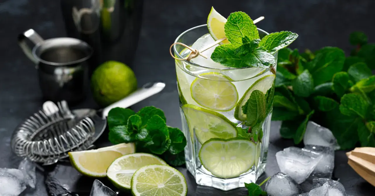 Szklanka orzeźwiającego mojito z limonką i miętą, otoczona lodem i składnikami.