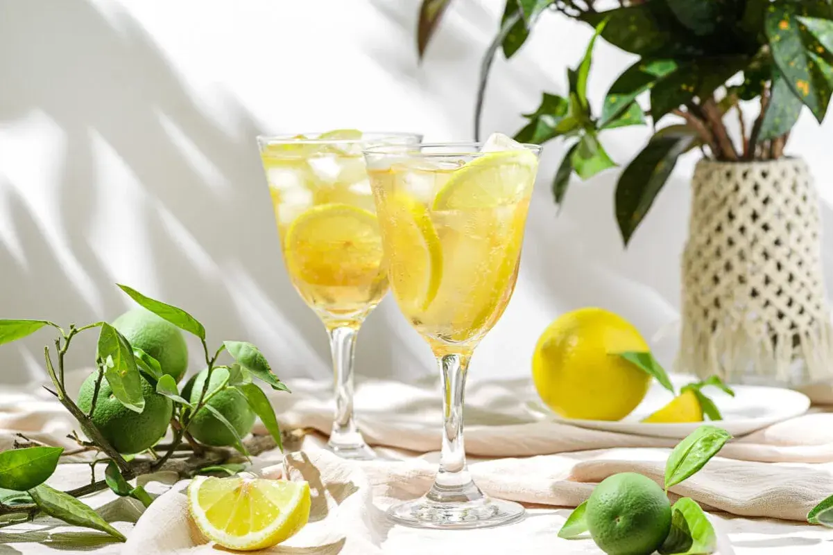 Orzeźwiający drink z limoncello, lodem i plasterkami cytryny, otoczony świeżymi owocami i zielonymi liśćmi.