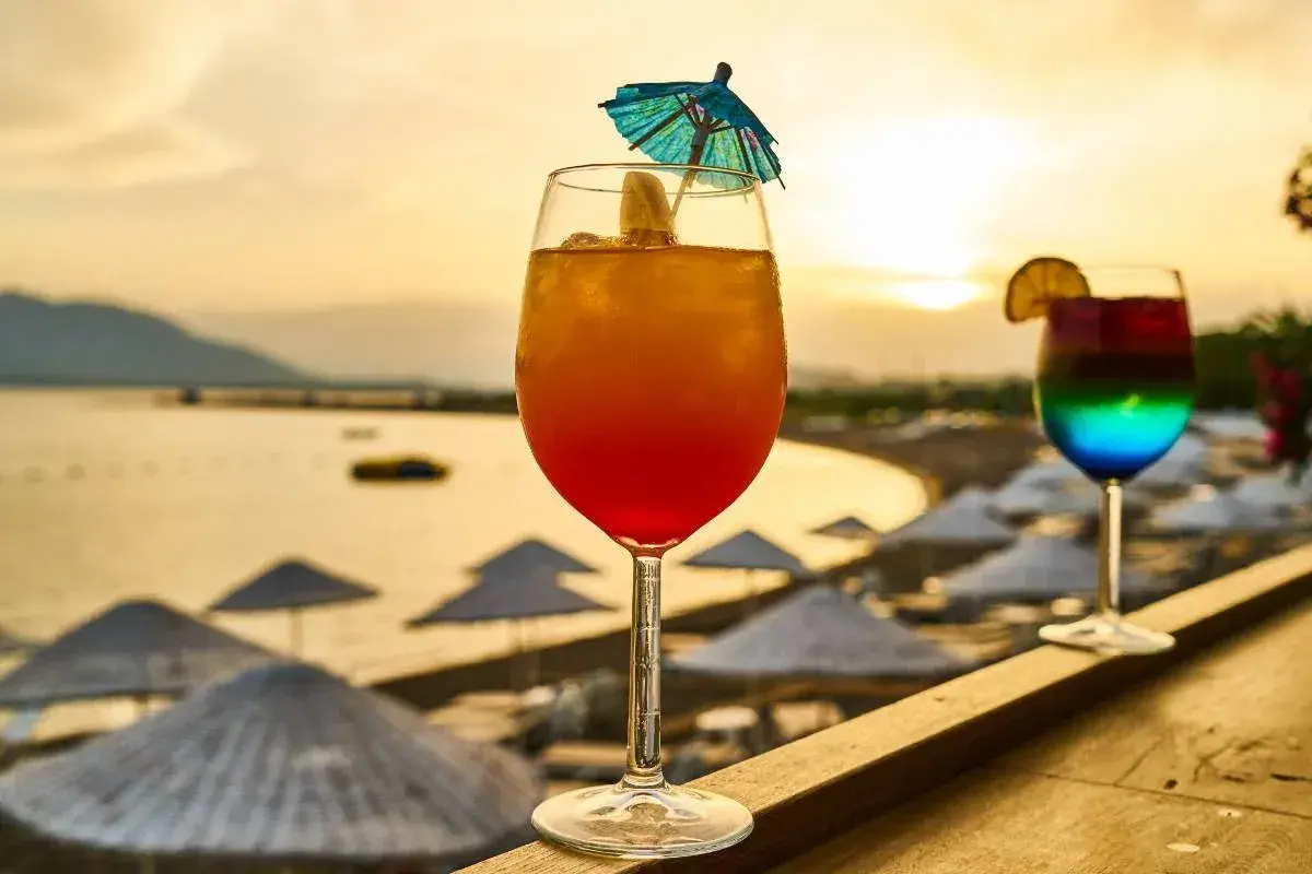 Dwa kolorowe drinki na tle plaży i zachodzącego słońca.