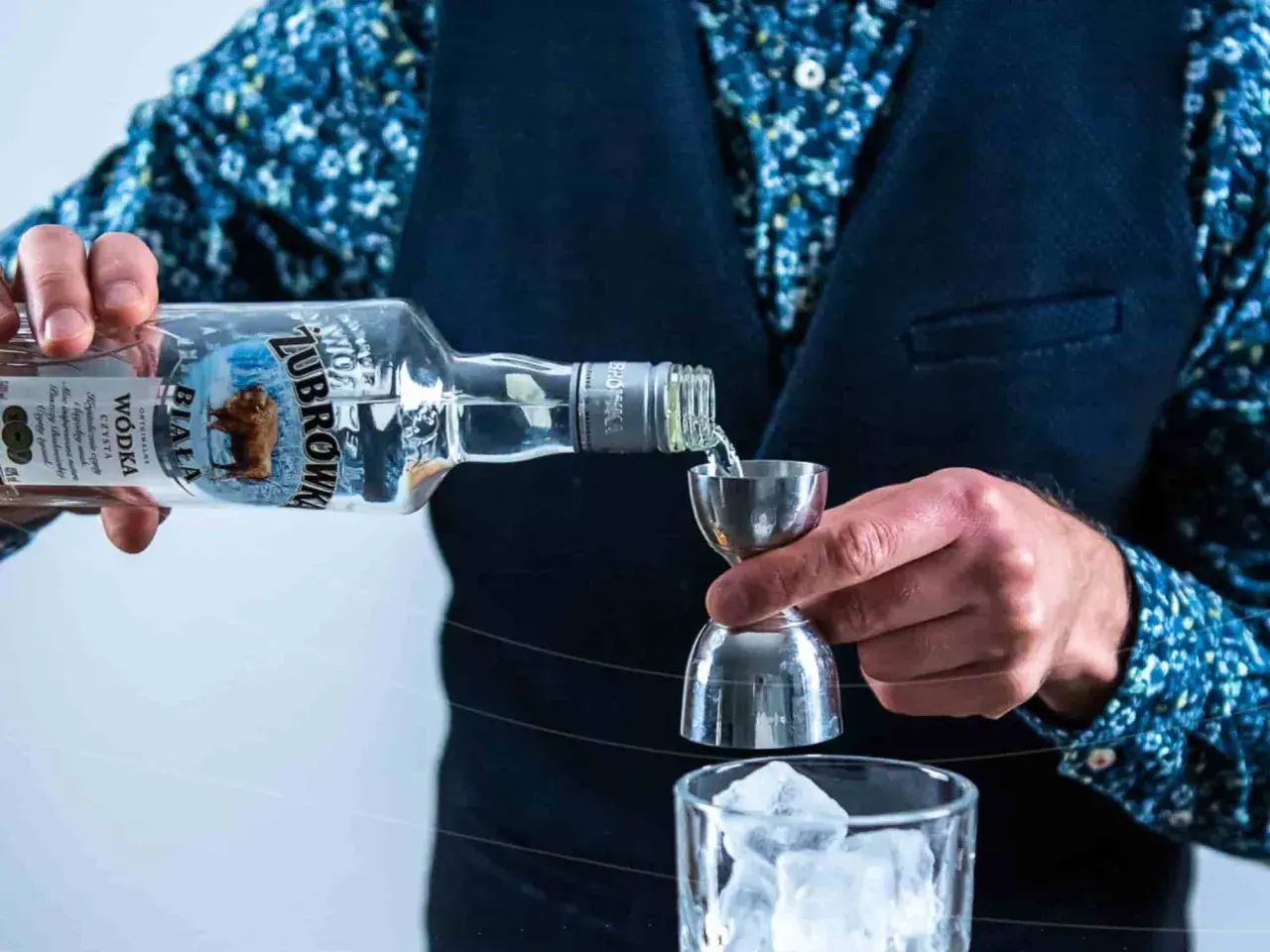 Barman nalewa wódkę Żubrówka Biała z butelki do jiggera nad szklankę z lodem.
