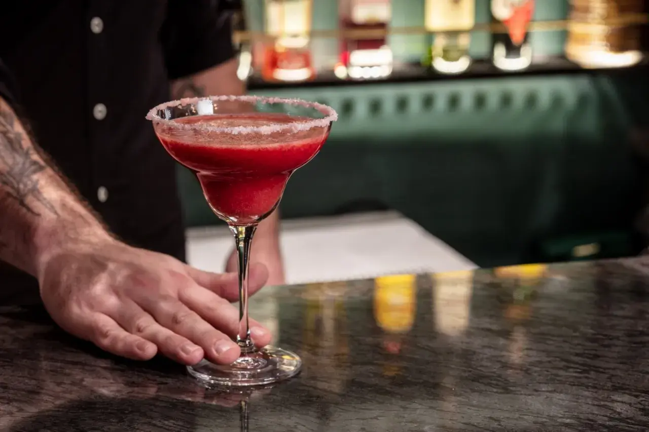 Mrożona czerwona margarita w kieliszku z solą na brzegu, podawana przez barmana.