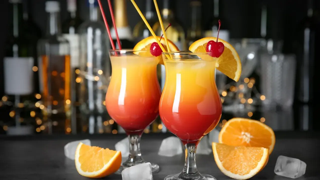 Dwa drinki z wódką w kieliszkach z pomarańczą i wiśnią, na tle baru.