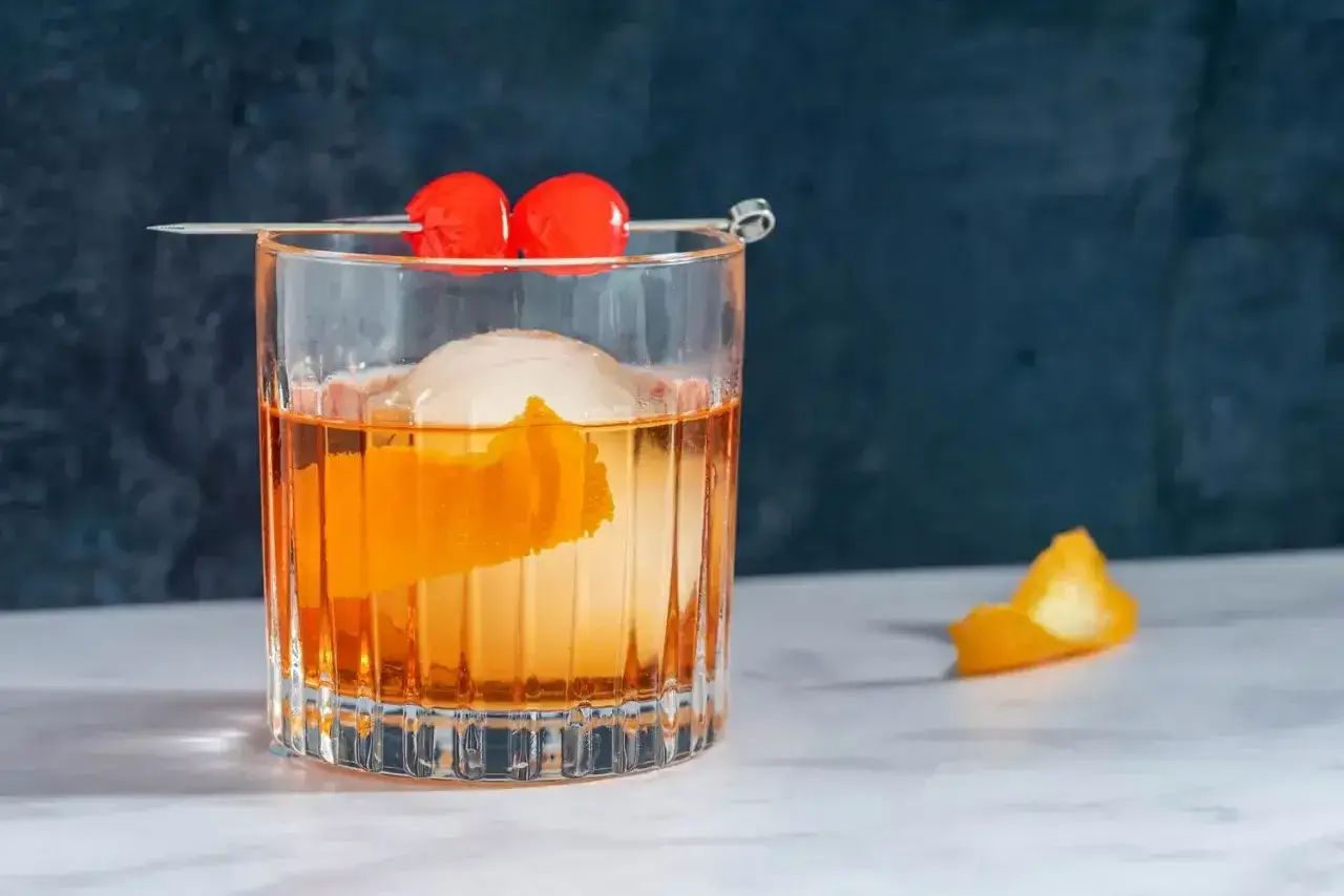 Klasyczny koktajl Old Fashioned z pomarańczą i wisienkami na patyczku.