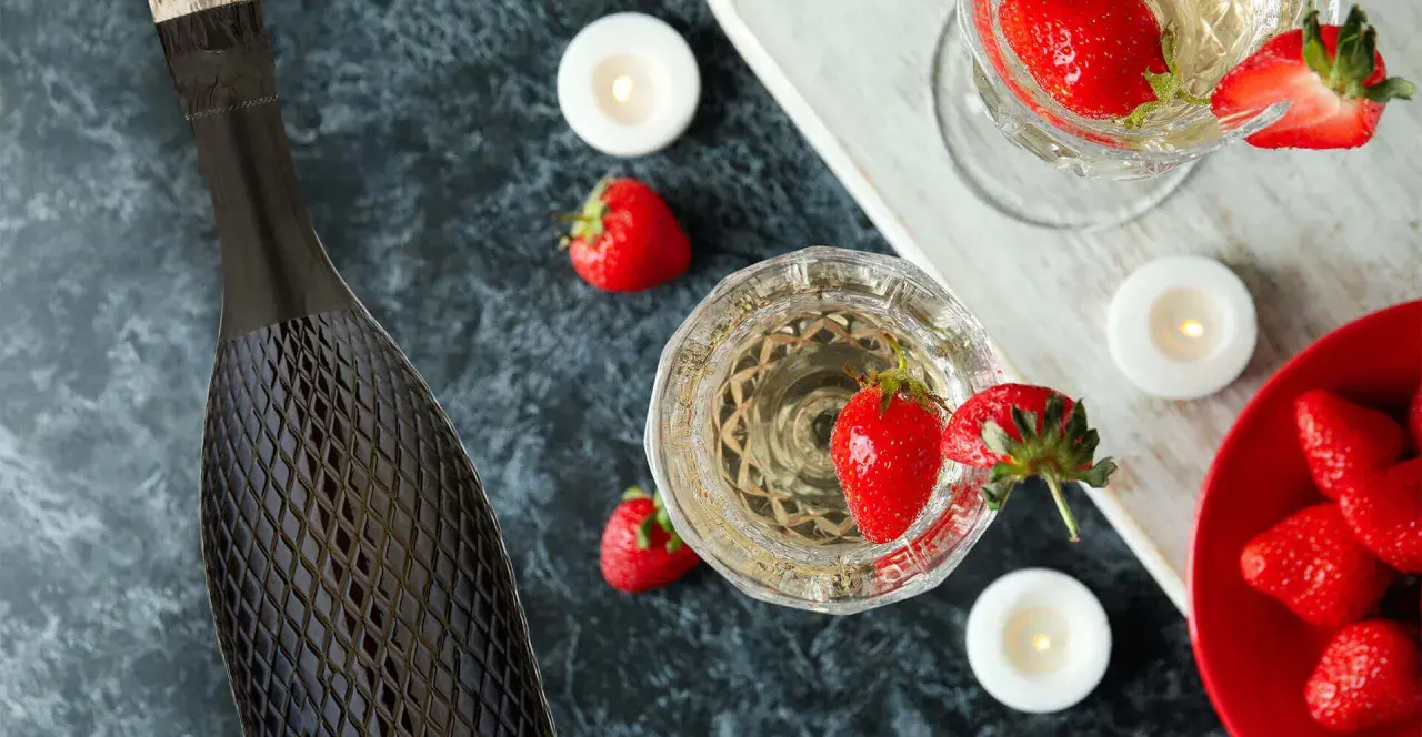 Butelka i kieliszki pełne musującego prosecco, ozdobione truskawkami i świecami. Idealne na romantyczny wieczór.