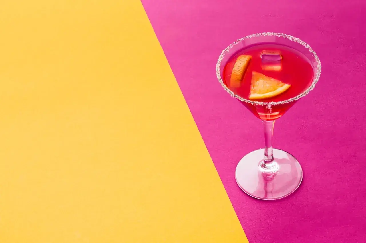 Elegancki kieliszek z czerwonym drinkiem, ozdobiony plasterkami pomarańczy i cukrowym rantem, idealny na wieczór w stylu cosmopolitan.